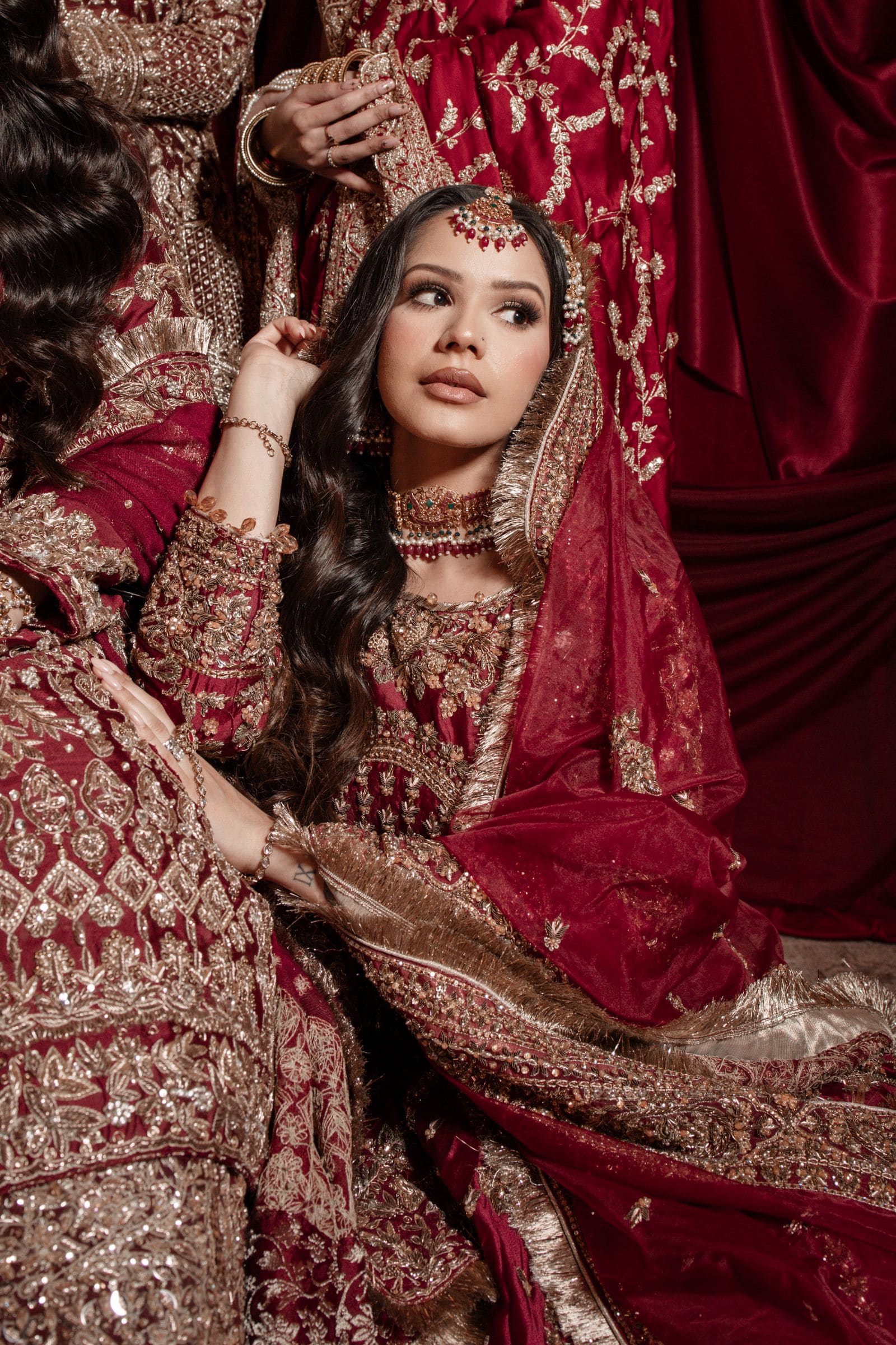 عارضة بطقم عنابي مطرّز، يدها عند الياقة
